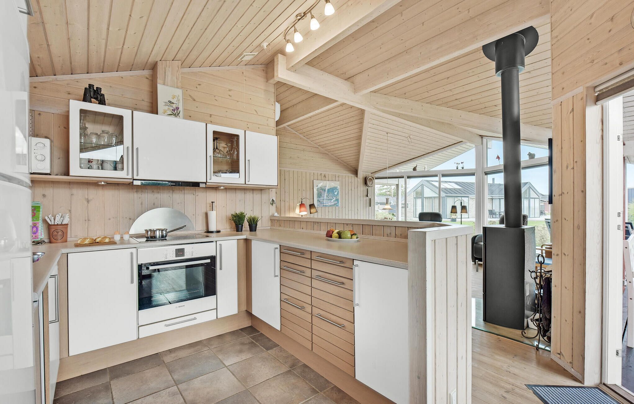 Une cuisine moderne avec des meubles blancs, un four Bosch et une grande fenêtre donnant sur un jardin.