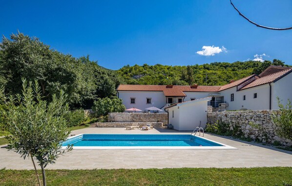 Ein zweistöckiges Haus mit Swimmingpool, Steinmauern und einem roten Ziegeldach.