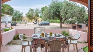 Een terras buiten met een eettafel, omringd door stoelen, en een uitzicht op de straat en geparkeerde auto's op de achtergrond.