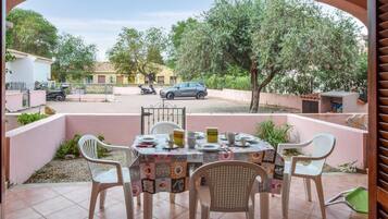 Una terrazza esterna con un tavolo apparecchiato per mangiare, circondata da sedie, e vista sulla strada e sulle auto parcheggiate sullo sfondo.