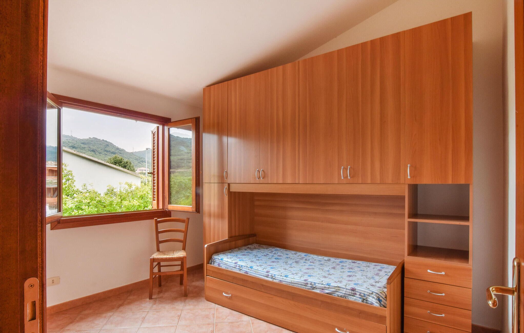 Ein Schlafzimmer mit Holzmöbeln, einem Fenster mit Blick auf Grünflächen und einem Sessel.