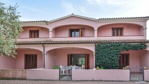 Een roze villa met drie bogen, een overdekte patio en een groene muur begroeid met klimop.