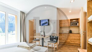 A hotel room with a bed, a desk with a chair, a TV, a kitchen area with a microwave, and a view of the outdoors. - schoene Ferienwohnung (Klösterle)