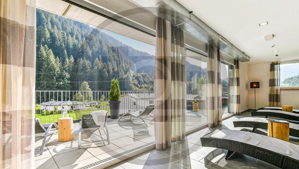 A modern hotel room with a large balcony, a dining area, and a view of a forested mountain range. - schoene Ferienwohnung (Klösterle)