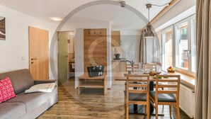 A modern living room with a sofa, a dining table with chairs, and a kitchen area in the background. - schoene Ferienwohnung (Klösterle)