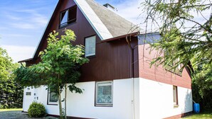 Ein zweistöckiges Haus mit einem steilen Satteldach, einem sichtbaren Schornstein und einem kleinen Fenster im Obergeschoss.
