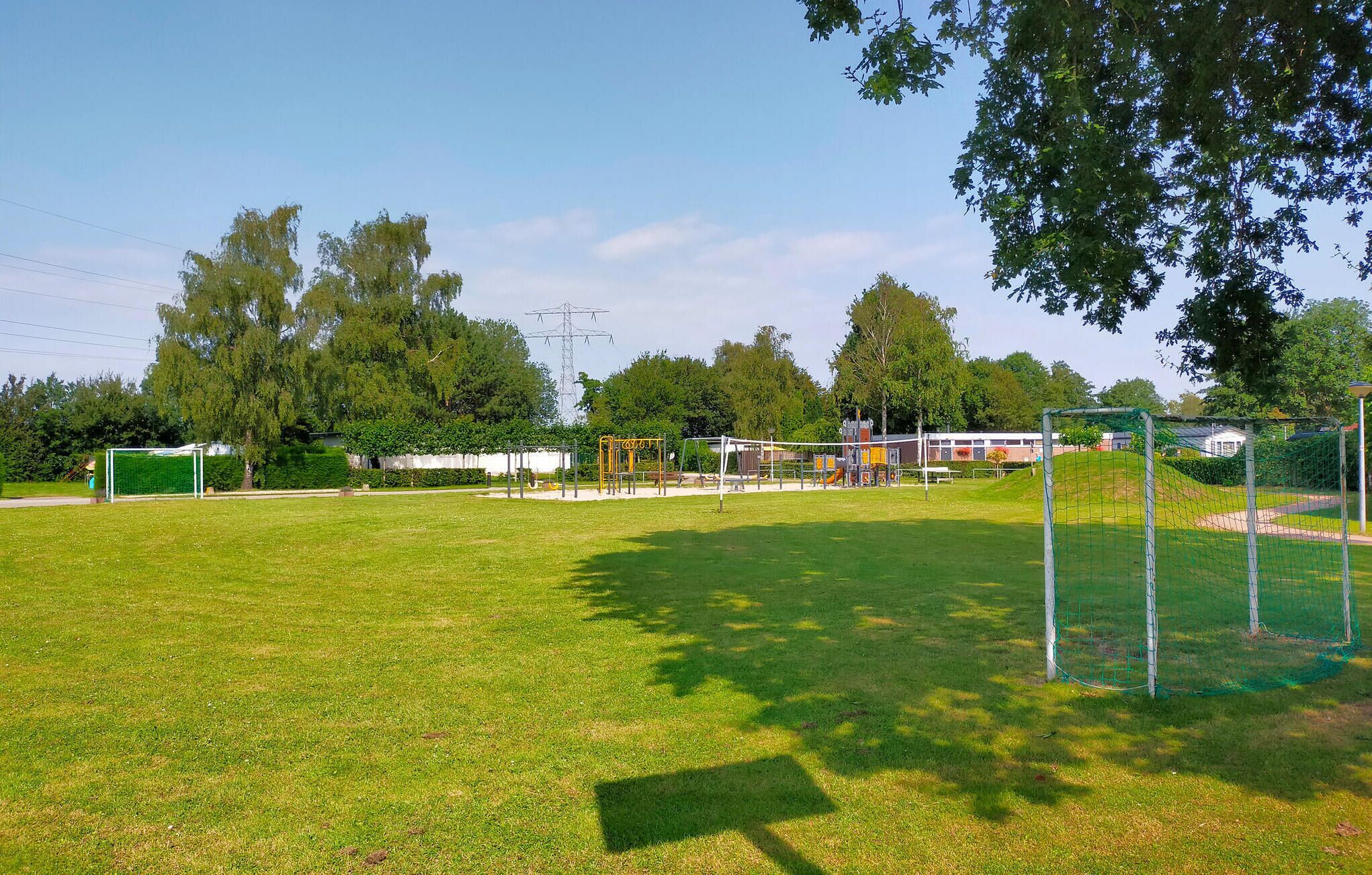 Een gazon met speeltoestellen, een voetbaldoel en bomen op de achtergrond.