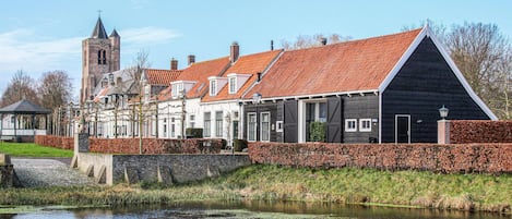 Un edificio histórico con tejado de tejas rojas, una torre y un canal frente a él.