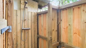 A wooden outdoor shower enclosure with a metal showerhead and hose.