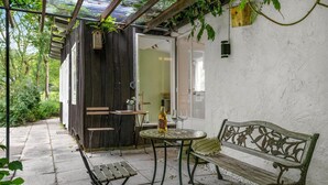 A patio with a wooden bench, a small round table, and a bottle of wine.