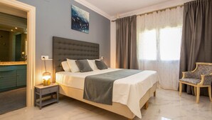 A bedroom with a large bed, a nightstand with a lamp, a chair, and a bathroom with a mirror and vanity. - Beautiful home in Mijas Costa with sauna (Mijas Costa)
