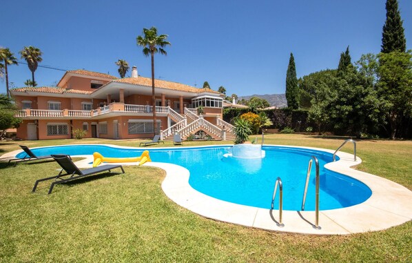 Ein Pool mit geschwungener Kante, umgeben von einem gepflegten Rasen. Liegestühle und eine Treppe, die zu einem Balkon führen.