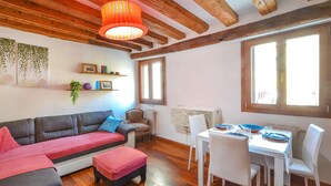 A cozy living room with a sofa, a dining table with chairs, wooden beams on the ceiling, and a large window. - Lovely apartment in Venezia with WiFi (Venezia)