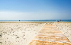 En strand med en træpromenade der fører ned til vandet, sand og en klar himmel.
