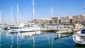 Un puerto deportivo con varias embarcaciones amarradas, un muelle y edificios residenciales al fondo.