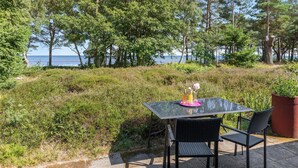 Ein Tisch mit Stühlen steht auf einer Terrasse mit Blick auf das Meer und Bäume.