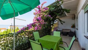 Ein Balkon mit Tisch und Stühlen, einem grünen Sonnenschirm und Blick auf das Meer.
