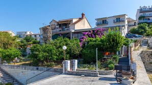 Ein Wohngebäude mit Balkon, umgeben von üppigem Grün und blühenden Pflanzen.