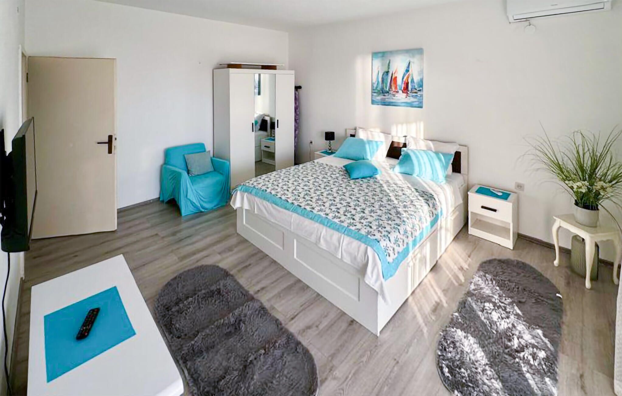 Une chambre à coucher moderne avec un lit, une chaise, une petite table, une table de chevet, une plante en pot et un tableau accroché au mur.