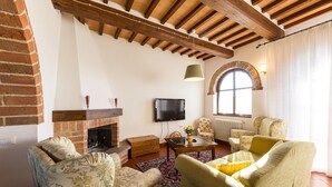 A cozy living room with a fireplace, floral armchairs, a television, and a large arched window. - Stunning home in Chiusi (Chiusi)