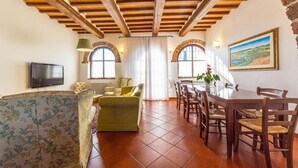 A spacious living room with a sofa, a dining table with chairs, a TV mounted on the wall, and a painting on the wall. - Stunning home in Chiusi (Chiusi)