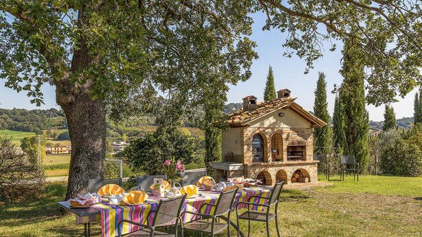 An outdoor dining area with a stone building, surrounded by trees and a grassy landscape. - Stunning home in Chiusi (Chiusi)