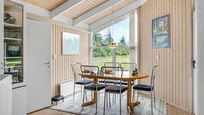 A dining area with a wooden table and chairs, a view of the outdoors, and a painting on the wall.