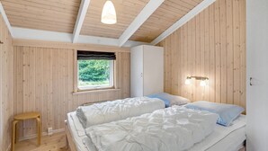 A bedroom with two beds, wooden walls, a window with a view of greenery, and a hanging light fixture.