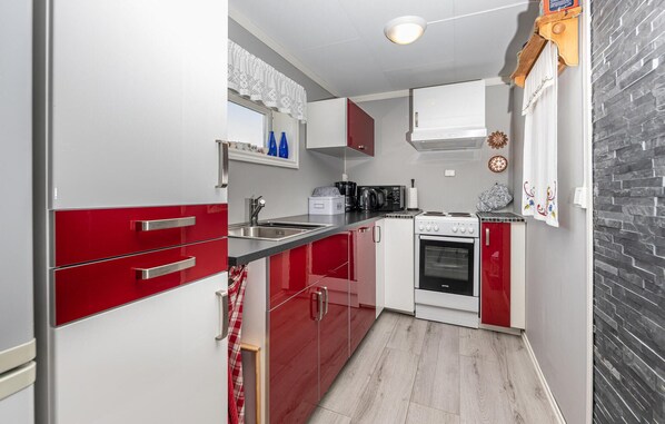 Une cuisine de taille réduite avec des meubles rouges et blancs, une cuisinière, un évier et une machine à café.