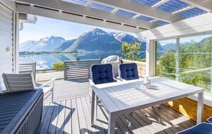 Une terrasse avec une table et des chaises, d’où l’on a vue sur un lac et des montagnes.