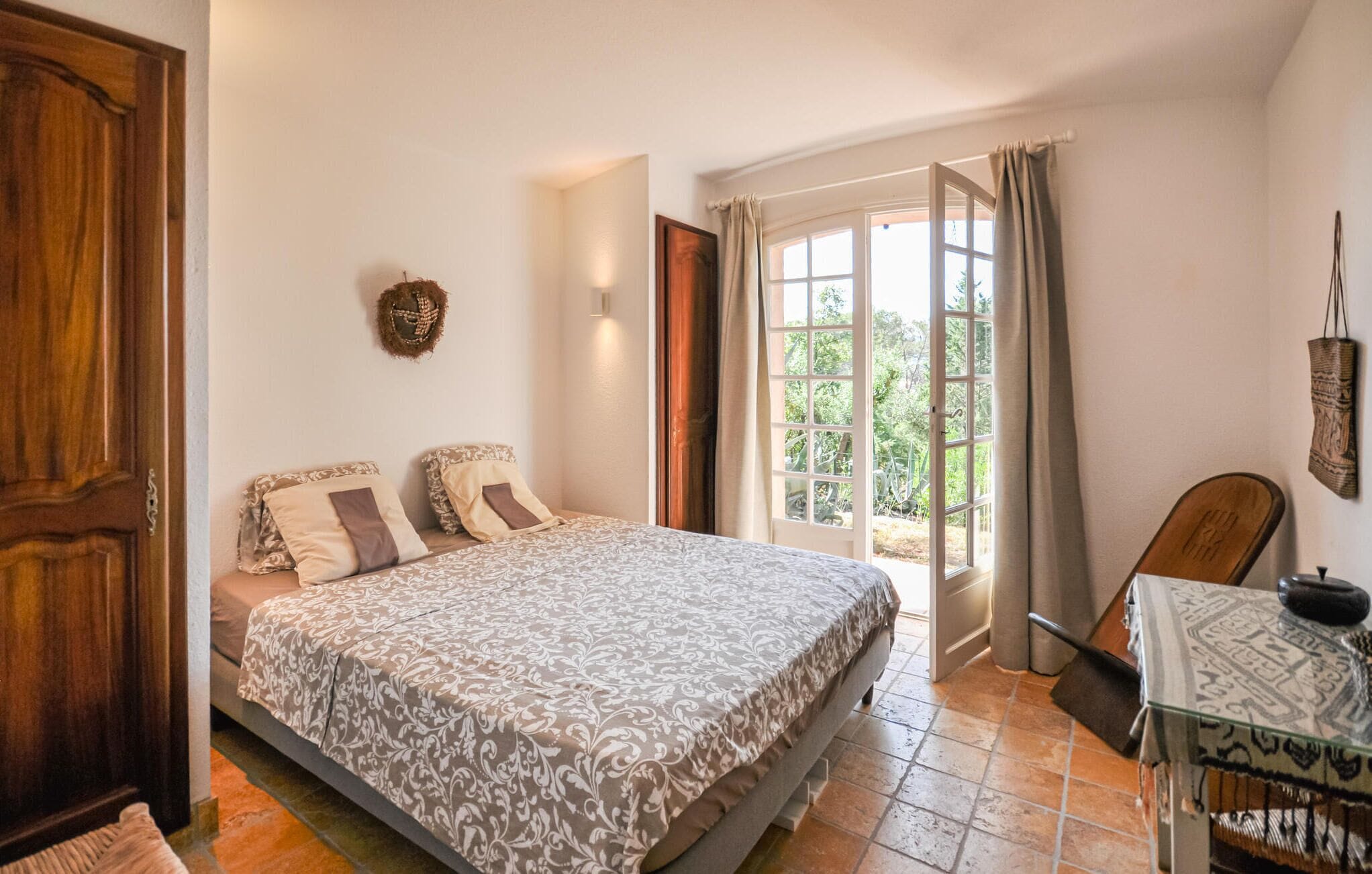 Une chambre à coucher avec un lit, une porte en bois, une fenêtre avec des rideaux et une petite table avec une chaise.
