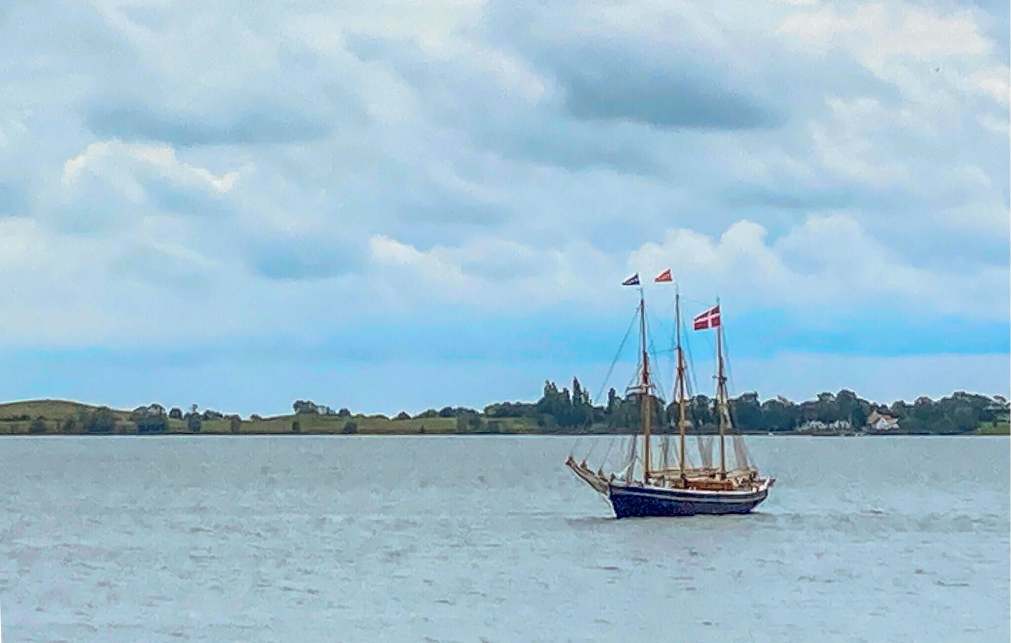 A sailboat on a body of water with a cloudy sky and a distant shoreline.