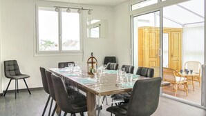 A dining area with a long table set for six, surrounded by chairs, with a view of a wooden cabinet and wicker chairs through a glass door. - 4 bedroom beautiful apartment in Pirou (Pirou)