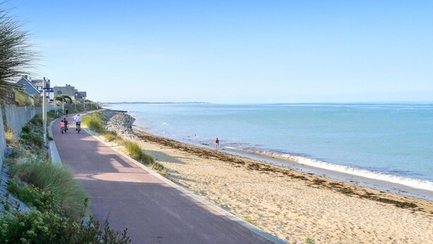 A coastal road with a beach on one side, a clear sky, and a few people walking or cycling. - 4 bedroom beautiful apartment in Pirou (Pirou)