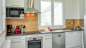 A modern kitchen with white cabinets, a Bosch microwave, a stainless steel range hood, a dishwasher, and a window providing natural light. - 4 bedroom beautiful apartment in Pirou (Pirou)