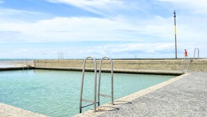 A swimming pool with metal ladders, a concrete deck, and a lifeguard tower in the background. - 4 bedroom beautiful apartment in Pirou (Pirou)