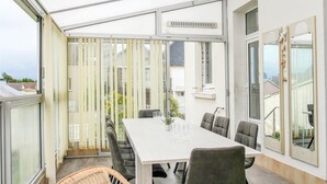 A modern outdoor dining area with a white table and grey chairs, surrounded by large windows and a white ceiling. - 4 bedroom beautiful apartment in Pirou (Pirou)