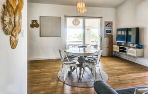 Un coin repas avec une table ronde et des chaises, un téléviseur posé sur un meuble, et une grande fenêtre donnant sur un beau paysage.