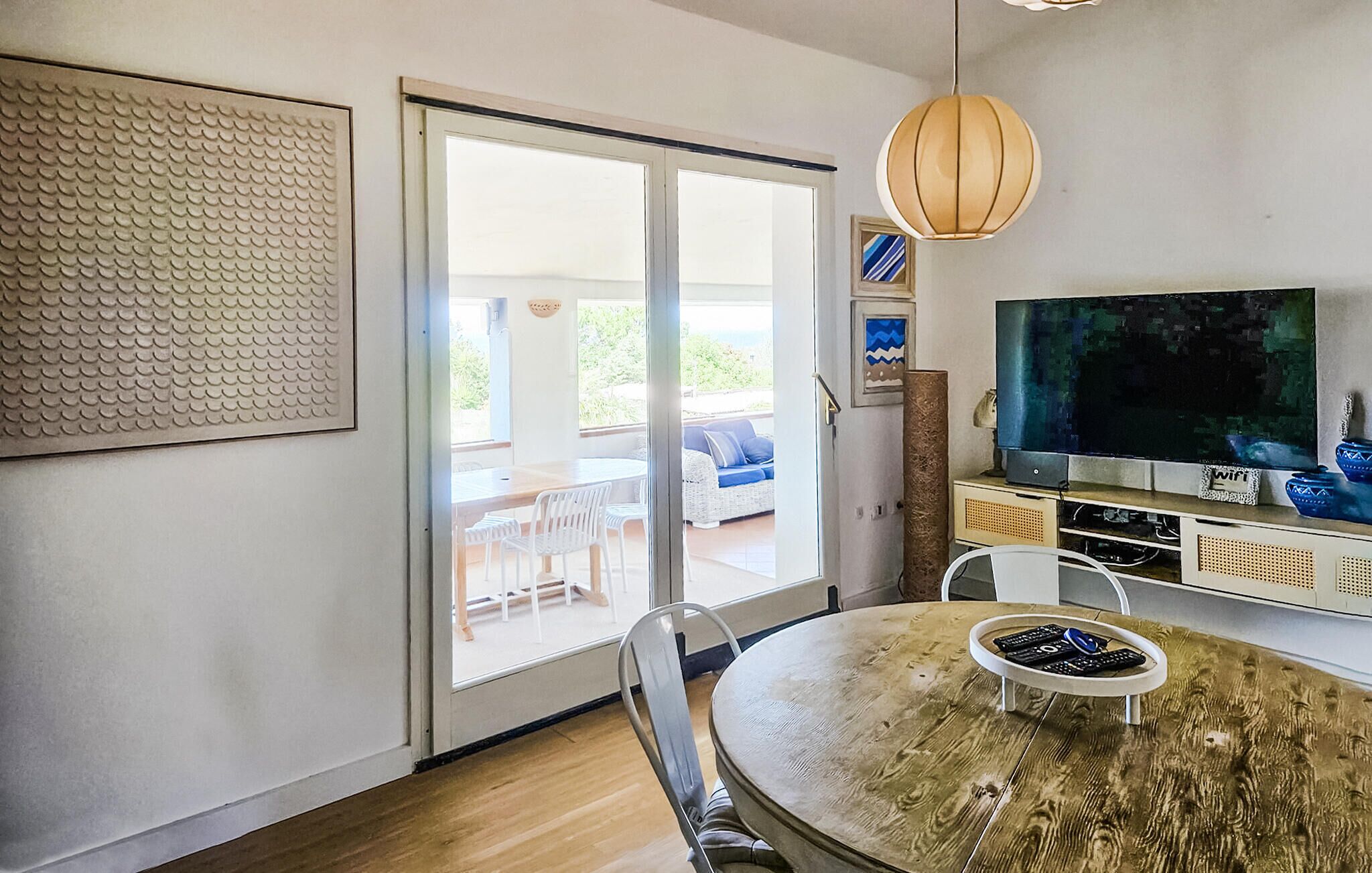 A room with a dining table, chairs, a television, and a sliding glass door leading to an outdoor area.