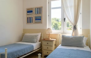 A bedroom with two single beds, a nightstand, a lamp, and a window with curtains.