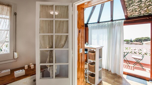 Ein Zimmer mit großem Fenster, Holztür und Blick auf einen Balkon mit Gartenmöbeln.