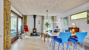 Un salon moderne avec une cheminée, un coin repas avec des chaises bleues et une grande fenêtre agrémentée de rideaux.