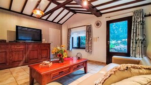 Una sala de estar con televisor, armarios de madera, una mesa de centro con flores, un sofá y una ventana con cortinas.