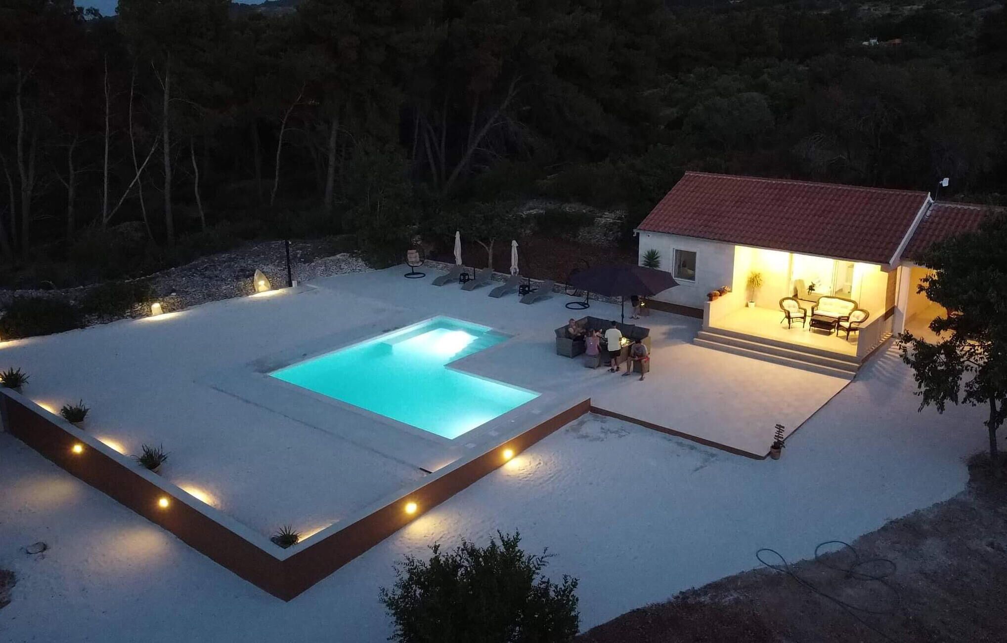 Ein Poolbereich mit einem Haus, Sitzgelegenheiten im Freien und einer gut beleuchteten Terrasse.