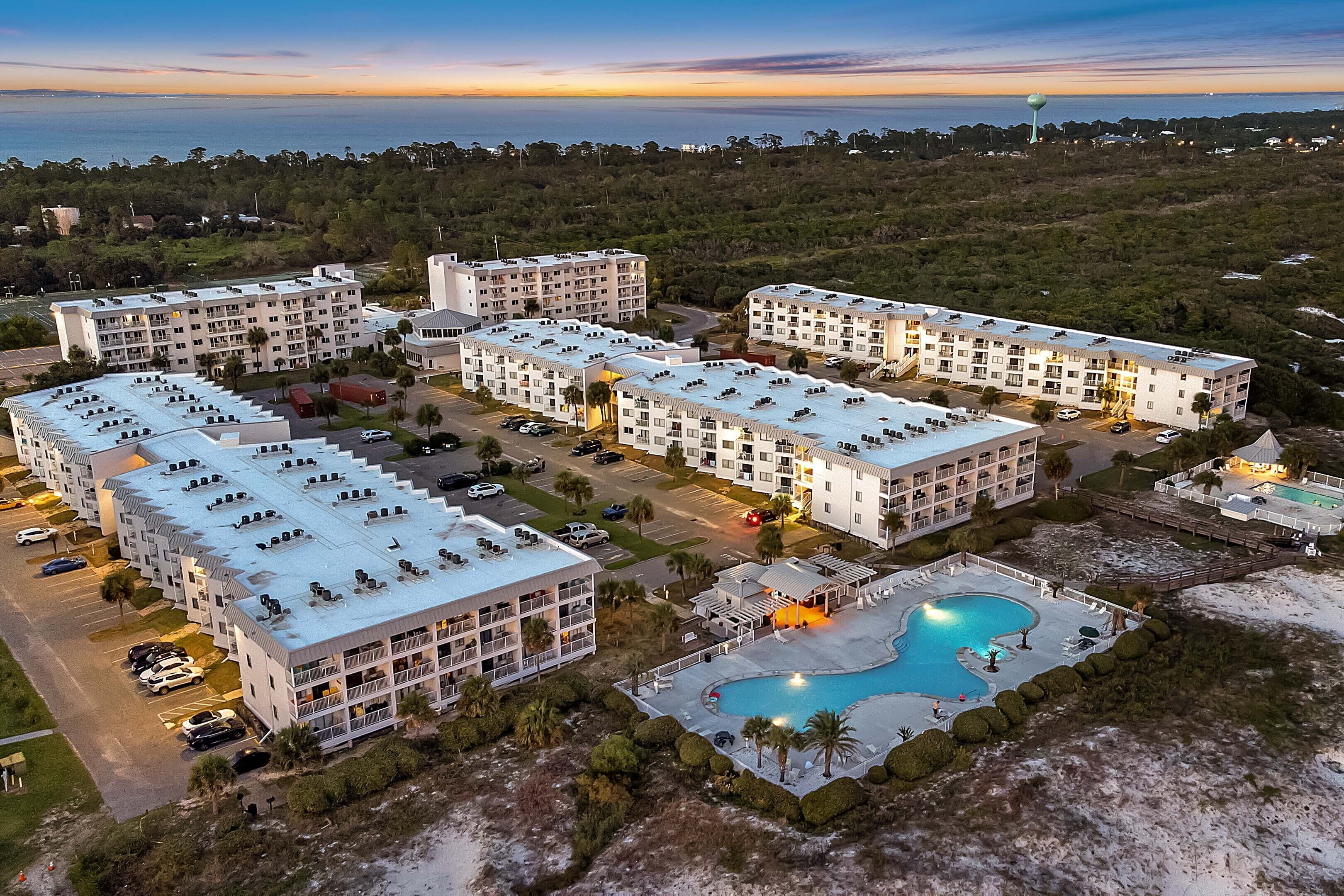A multi-story hotel with a swimming pool, parking areas, and a view of the ocean.