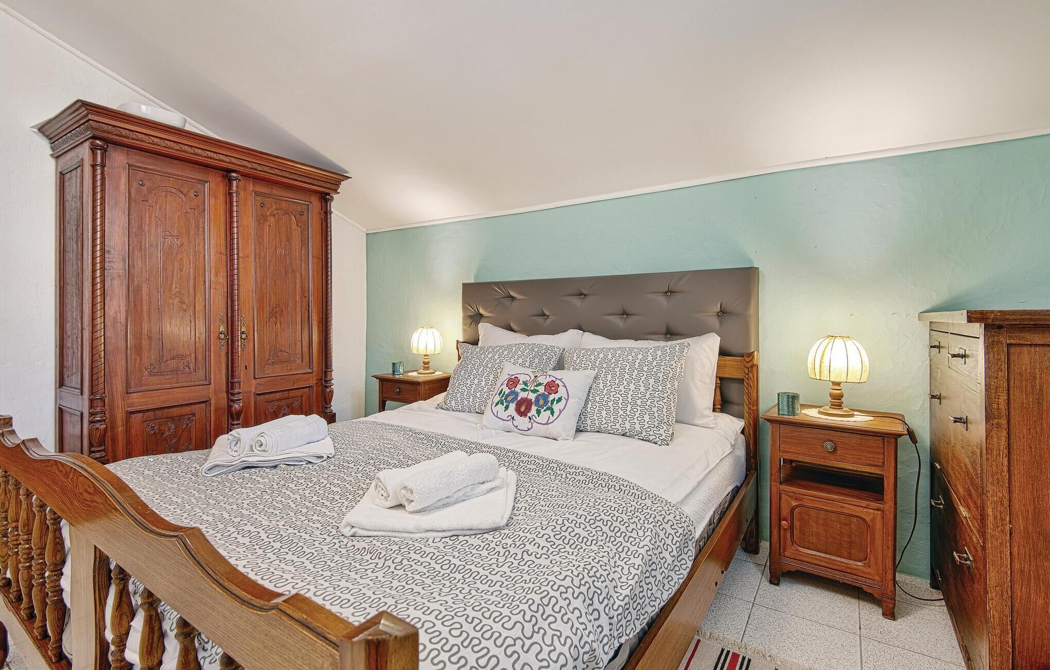Una cama bien hecha con ropa de cama estampada, dos mesitas de noche con lámparas y un armario de madera.