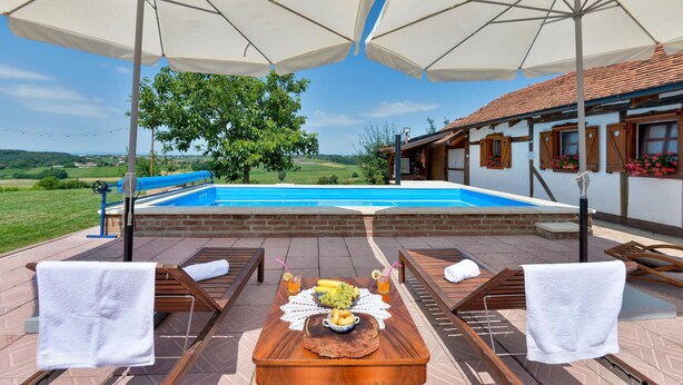 Ein Poolbereich mit Blick auf ein Schwimmbecken, ein Holztisch mit Früchten und Getränken sowie Liegestühle mit Handtüchern.