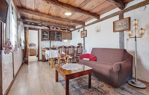 Een gezellige woonkamer met een houten plafond, een rode bank, een eettafel met stoelen en een kamerbreed tapijt met dessin.