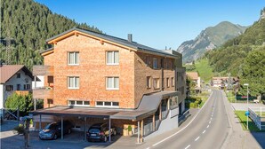 Un edificio a più piani con facciata in mattoni, un'area di parcheggio coperta e una strada che conduce in una zona montuosa.
