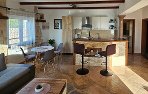 A cozy living room with a sofa, a dining table with chairs, a kitchen area with a bar, and a stone fireplace. - Cozy apartment in Rovanjska / Jasenice with WiFi (Rovanjska / Jasenice)